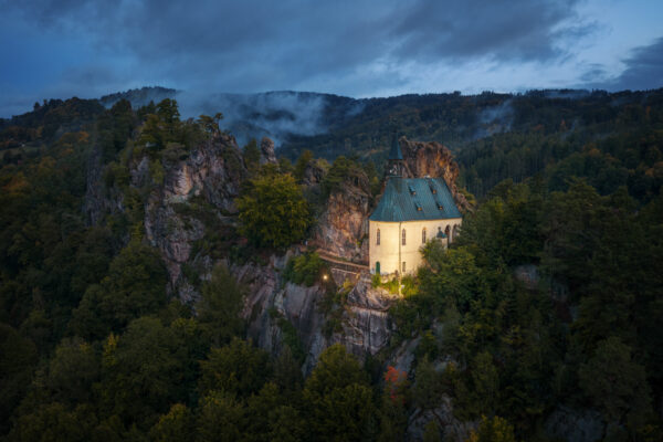 This chapel rests atop a rock, embraced by a sea of trees and silent mist. A place of peace and resilience, where nature and spirit meet. -