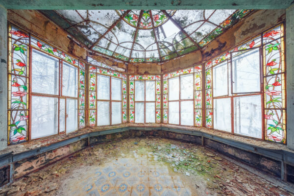 In this abandoned conservatory, the intricate glasswork still captures the imagination, a silent testament to a space once filled with life and light. -